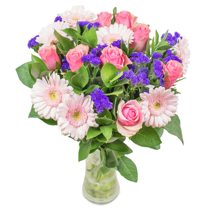 This richly detailed bouquet, arranged in a transparent glass vase and set against a pristine white background, is a celebration of Oxted's vibrant character and gardening heritage. At its heart are seven to nine pink roses, their petals stiffly furled or just beginning to open, each bearing the classic spiral form that hints at timeless romance. These are complemented by five to seven pale pink gerbera daisies, their large faces and radiant petals glowing with subtle beauty, each centre almost dusted with white like blossoms in the spring meadows near Limpsfield Common. Vibrant purple statice is artfully woven through the bouquet, providing striking texture and deep color, while lush, deep green foliage supplies a base reminiscent of Oxted's leafy avenues. The slender, crystal-clear vase reveals the clean lines of the stems and glistening water, a finishing touch worthy of a fresh flower delivery from Flowers Oxted. Whether placed in a welcoming hallway on Gresham Road, as a heartfelt anniversary gift, or as a tasteful accent to an office reception, this arrangement brings together joyful colour, freshness, and the affection characteristic of Oxted's community spirit.